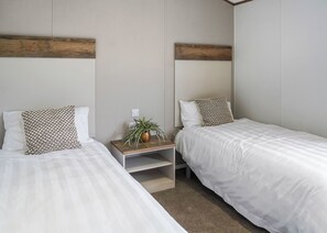 Habitación doble con dos camas, una mesita de noche con una planta y un cabecero de madera.