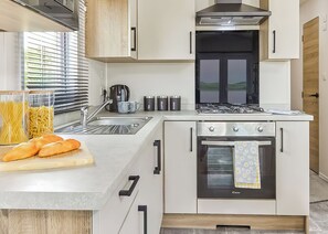 A compact kitchen with a gas stove, oven, and a sink. - Signature 2 Bed Caravan Wheelchair Accessible (Ormside, Appleby-in-Westmorland)