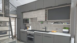 A modern kitchen with grey cabinetry, a built-in stove, a microwave, and a sink. There is a wooden staircase leading to an upper level.