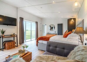 Une chambre moderne avec un grand lit, un téléviseur à écran plat, une table de chevet, un miroir et une vue sur l’extérieur.