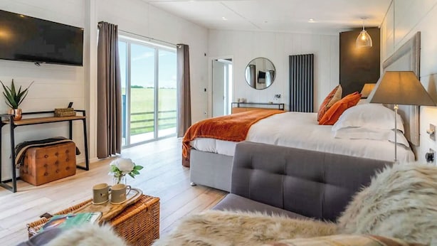 Un dormitorio moderno con una cama grande, un televisor de pantalla plana, una mesita de noche, un espejo y vistas al exterior.