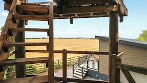 Una terraza de madera con barandilla de metal, una escalera de madera y vistas a un campo.