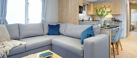 A modern living room with a sectional sofa, a dining area, and a kitchen in the background.