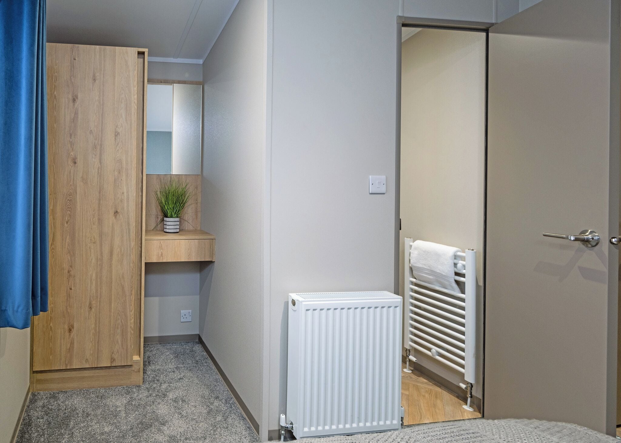 A room with a wardrobe, a radiator, a towel rack, and a small plant on a shelf.