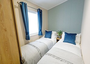 Un dormitorio con dos camas, una ventana con cortinas, una mesita de noche con una planta y una puerta de madera.