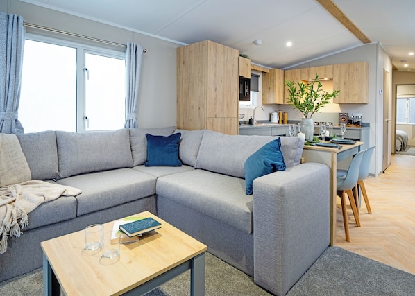 A modern living room with a sectional sofa, a dining area, and a kitchen in the background.