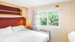 Une chambre d’hôtel avec un lit, une fenêtre donnant sur un espace verdoyant, un radiateur et une étagère fixée au mur.