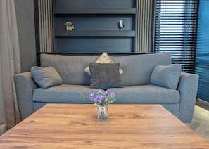 A grey sofa with a vase of purple flowers on a wooden coffee table. - 1 bedroom accommodation in Millom (Millom)