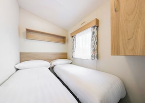 A bedroom with two beds, a wooden headboard, a shelf, and a window with curtains.