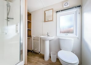 A bathroom with a toilet, sink, shower, and a window.