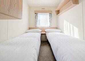 A compact room with two single beds, a window with curtains, and a wooden headboard.