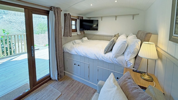 Un dormitorio con cama, televisor, lámpara y vistas al exterior.