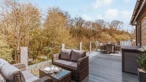 Um terraço com mobiliário de vime, uma mesa de centro de vidro e vista para árvores e um edifício.