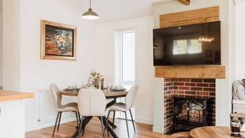 A dining area with a brick fireplace, a TV mounted above it, and a painting on the wall.