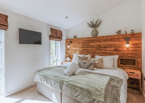 Une chambre à coucher avec une tête de lit en bois, un téléviseur à écran plat, une table de chevet avec une lampe et une fenêtre avec des rideaux.