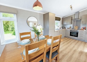 A modern kitchen with wooden cabinets, a built-in oven, and a dining area with a wooden table and chairs.