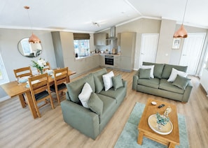A modern living space with a dining area, two sofas, a kitchen, and a large window.