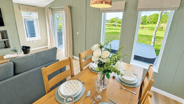 A dining area with a wooden table set for four, a sofa, and a view of a green landscape through large windows. - 2 bedroom accommodation in Market Bosworth, near Nuneaton (Market Bosworth, near Nuneaton)