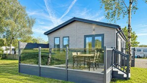 A modern wooden cabin with a glass-enclosed deck, outdoor seating, and a clear view of the surrounding greenery. - 2 bedroom accommodation in Market Bosworth, near Nuneaton (Market Bosworth, near Nuneaton)