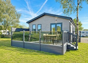 A modern wooden cabin with a glass-enclosed deck, outdoor seating, and a clear view of the surrounding greenery.