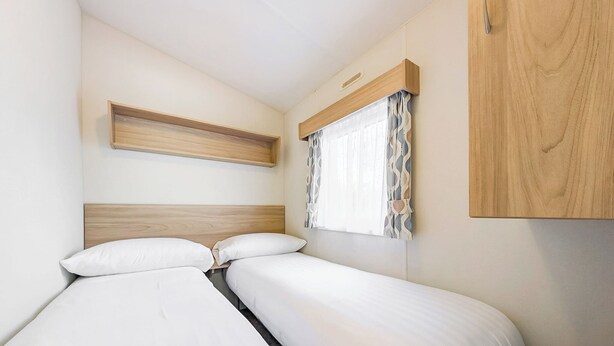 Quarto com duas camas, cabeceira de madeira, prateleira e janela com cortinas.