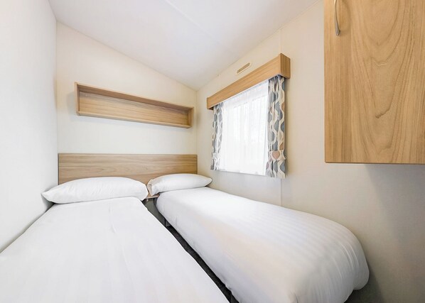 Un dormitorio con dos camas, cabeceros de madera, una estantería y una ventana con cortinas.