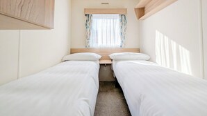 Quarto compacto com duas camas de solteiro, janela com cortinas e cabeceira de madeira.