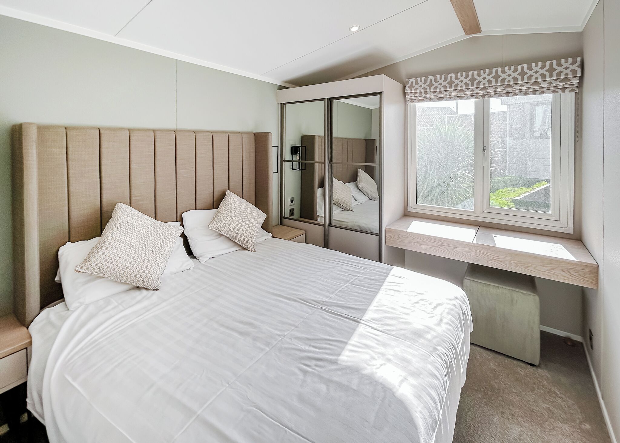 A bedroom with a bed, bedside tables, a wardrobe, a window with a view, and a mirror.