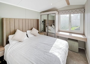 A bedroom with a bed, bedside tables, a wardrobe, a window with a view, and a mirror. - 4 bedroom accommodation in Bacton-on-Sea (Bacton-on-Sea)