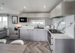 A modern kitchen with white cabinets, a gas stove, a microwave, and a toaster. - 4 bedroom accommodation in Bacton-on-Sea (Bacton-on-Sea)