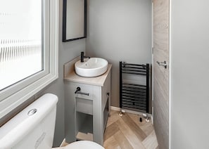 A compact bathroom with a white toilet, a sink with a black faucet, a mirror above the sink, and a towel rack. - 4 bedroom accommodation in Bacton-on-Sea (Bacton-on-Sea)