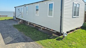 A single-story mobile home with a porch, a small deck, and a view of the water.