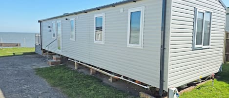 A single-story mobile home with a porch, a small deck, and a view of the water.