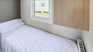A single bed with white bedding, a window with a view of a house, and a wooden panel on the wall.