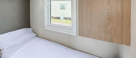 Ein Einzelbett mit weißer Bettwäsche, ein Fenster mit Blick auf ein Haus und ein Holzpaneel an der Wand.