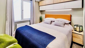 Une chambre à coucher comprenant un lit, une table de chevet, une fenêtre avec des rideaux et des armoires en bois intégrées au-dessus du lit.