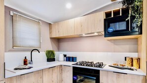Une cuisine moderne avec des meubles en bois, une cuisinière à gaz, un four, un four à micro-ondes et une fenêtre avec des stores.