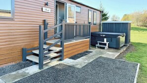 Une maison mobile en bois, dotée d’une véranda, d’un jacuzzi et d’une pancarte indiquant « Plage ».