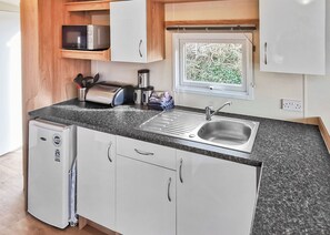 A compact kitchenette with a stainless steel sink, a microwave, a toaster, and a small refrigerator. - Gold Plus 3 Sleeps 6 (New Quay)
