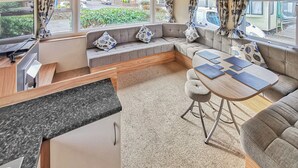 A compact RV interior with a kitchen area, seating, and a dining table. - Gold Plus 3 Sleeps 6 (New Quay)