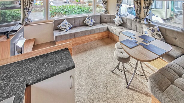 A compact RV interior with a kitchen area, seating, and a dining table. - Gold Plus 3 Sleeps 6 (New Quay)