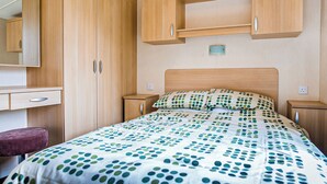 A bedroom with a bed, a desk, a chair, and wooden cabinets. - Gold Plus 3 Sleeps 6 (New Quay)