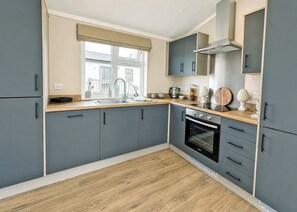 A modern kitchen with grey cabinets, a wooden countertop, a built-in oven, and a window with a valance.