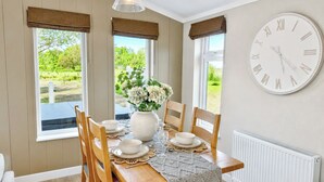 A dining area with a table set for four, a large wall clock, and a view of greenery outside. - 2 bedroom accommodation in Market Bosworth, near Nuneaton (Market Bosworth, near Nuneaton)