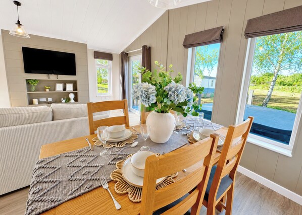 A dining area with a table set for four, a sofa, a television, and a view of the outdoors.