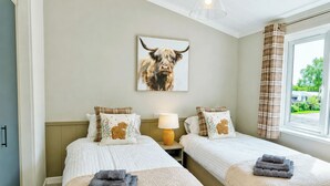 A hotel room with two beds, a lamp, a painting of a bull, and a window with curtains. - 2 bedroom accommodation in Market Bosworth, near Nuneaton (Market Bosworth, near Nuneaton)