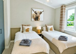 A hotel room with two beds, a lamp, a painting of a bull, and a window with curtains.