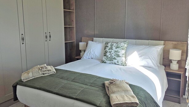 Habitación de hotel con una cama grande, un armario, una mesita de noche con lámpara y una ventana.