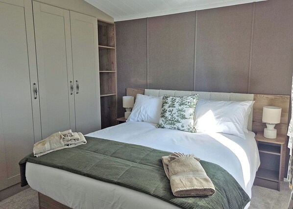 Habitación de hotel con una cama grande, un armario, una mesita de noche con lámpara y una ventana.