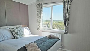 Un dormitorio con cama, ventana con cortinas, radiador y vista a la vegetación.